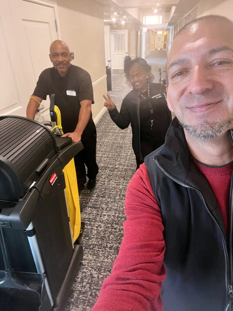 Three coworkers posing for a selfie in a hallway, capturing a fun moment together while working on spring cleaning at the community.