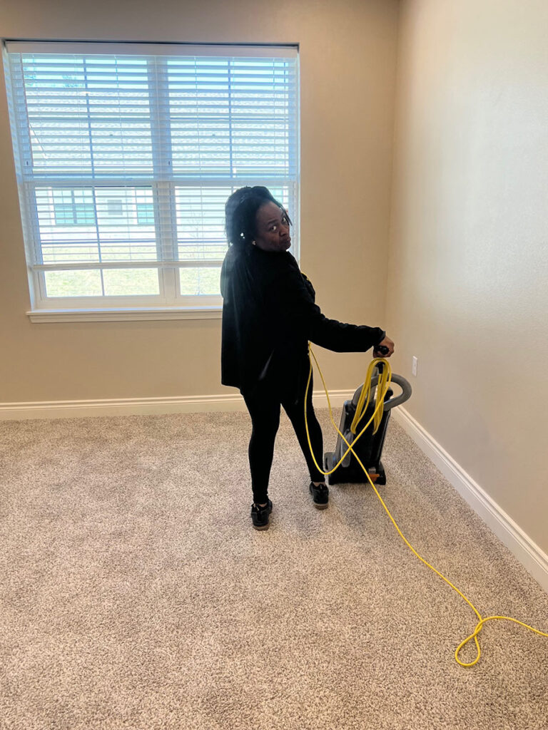 A woman vacuuming an empty apartment with a vacuum cleaner.