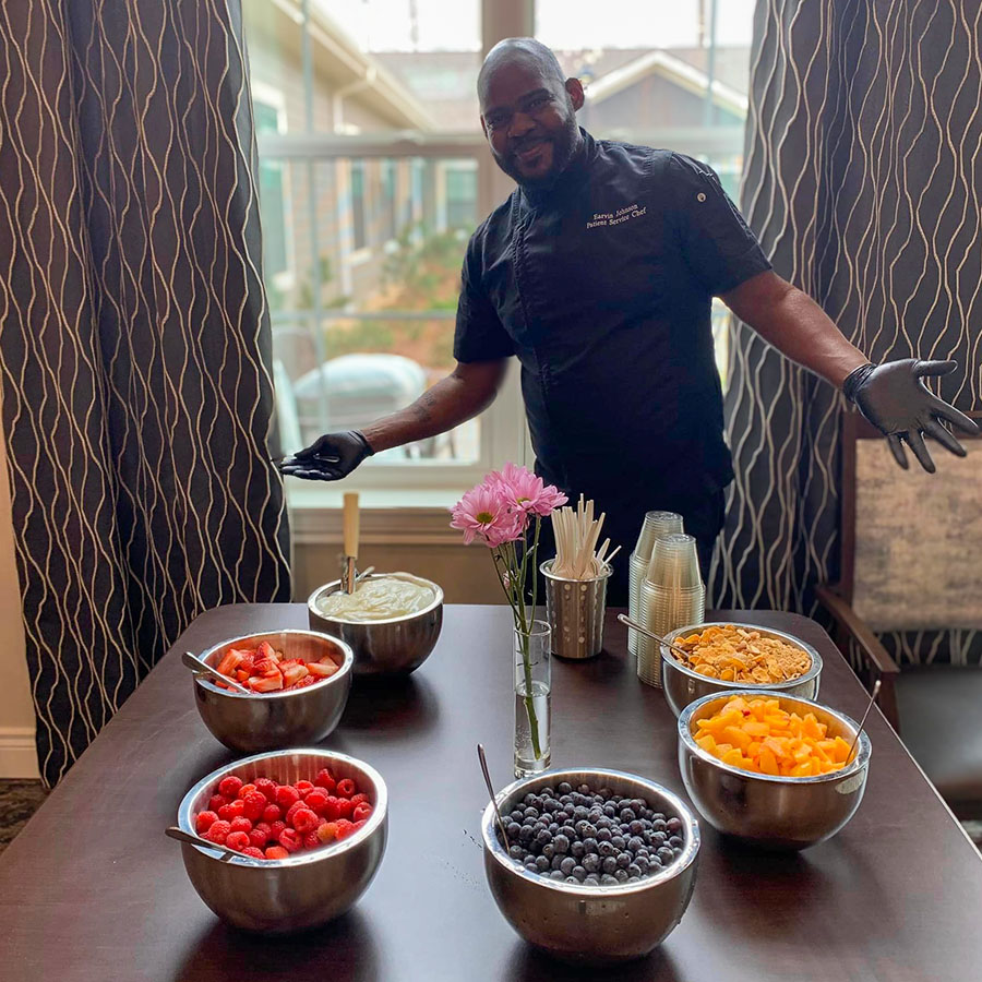 Wellness Wednesday's success with a culinary employee standing in front of colorful fresh fruit bowls at the Yogurt Bar event for residents.