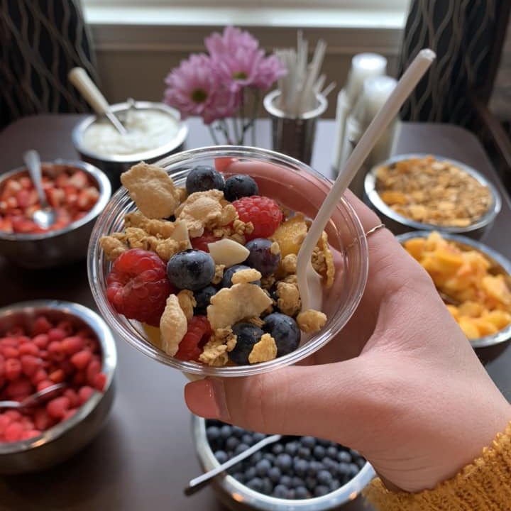 A delightful bowl of fruit and cereal held by a person at the Yogurt Bar, celebrating Wellness Wednesday with fresh and healthy choices!