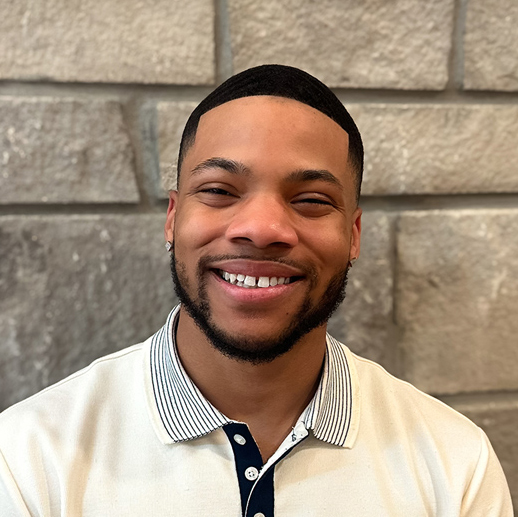 Kaleon Patterson, Senior Living Coordinator at The Summit Senior Living, smiles warmly in a light collared shirt, standing in front of a stone wall backdrop.