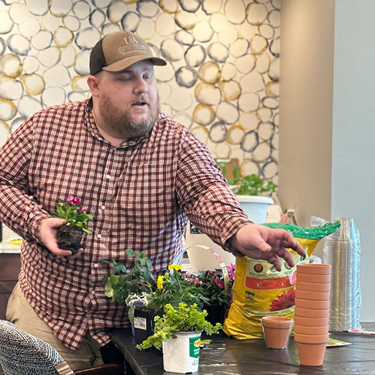 A local business owner pots plants with care, reaching for a stack of small terracotta pots.