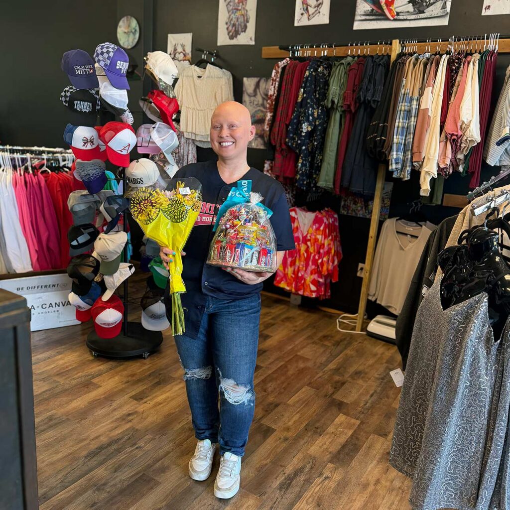 A small business owner smiles, holding flowers and a gift basket given by The Summit Senior Living.