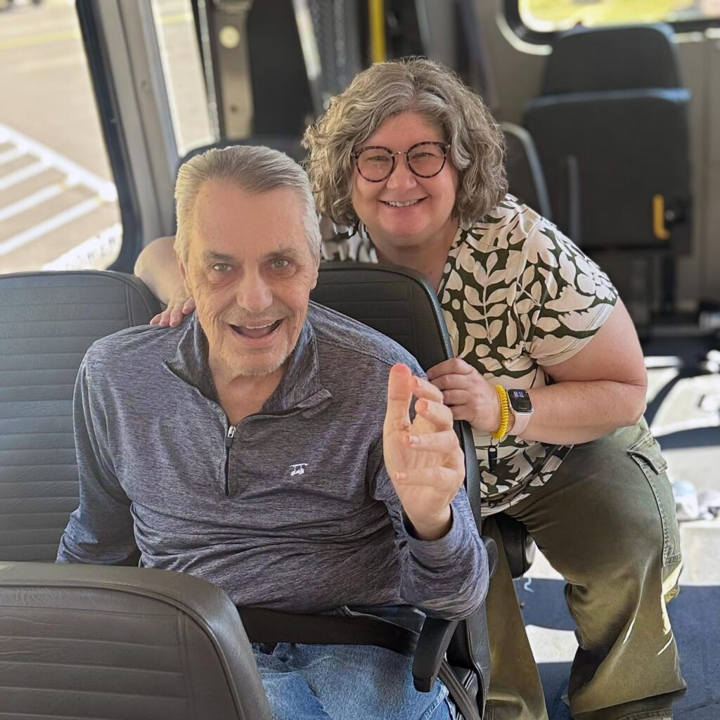 A woman and senior man smile widely in the Summit Senior Living's transport vehicle.