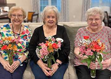 Three women on the Resident Ambassador team at The Summit Senior Living smile while holding flower bouquets.